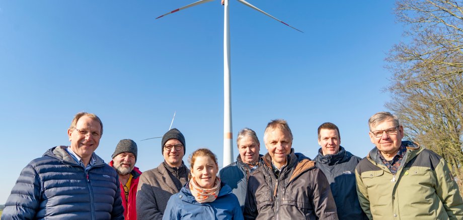 Several people stand in front of a wind turbine