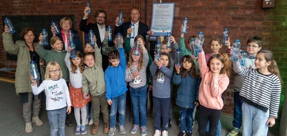 Schulkinder und vier Erwachsene stehen um einen Trinkwasserspender.