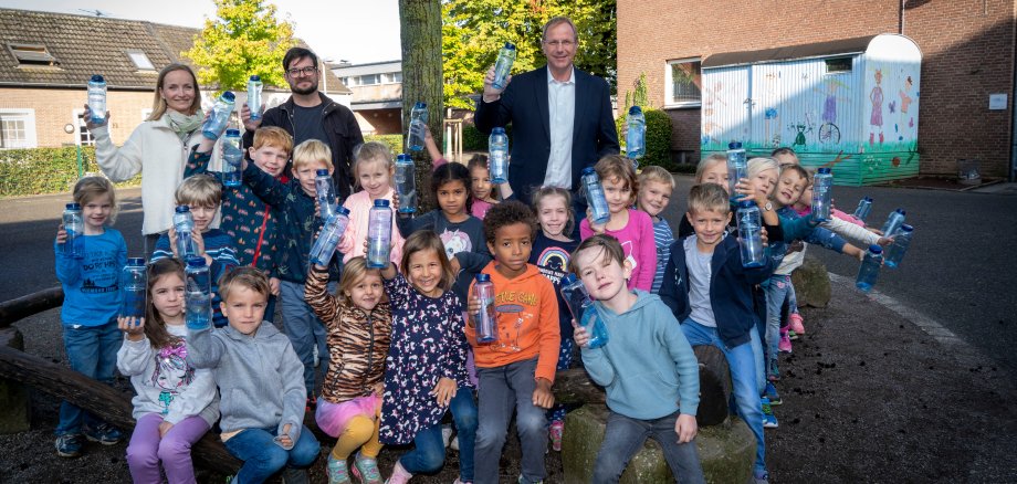 Zahlreiche Kinder und drei Erwachsene halten Trinkflaschen in die Kamera. 