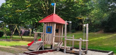 Ein großes Holz-Klettergerüst mit einem Sandkasten auf einem Spielplatz.